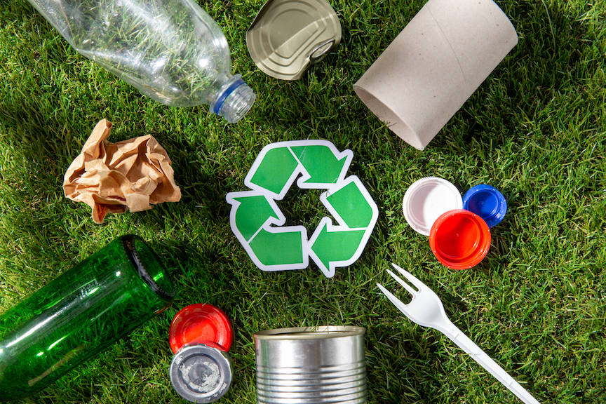 recycling, sustainability and ecology concept - green recycle sign with household waste on grass