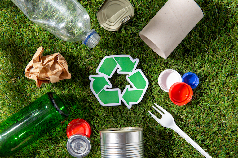 recycling, sustainability and ecology concept - green recycle sign with household waste on grass